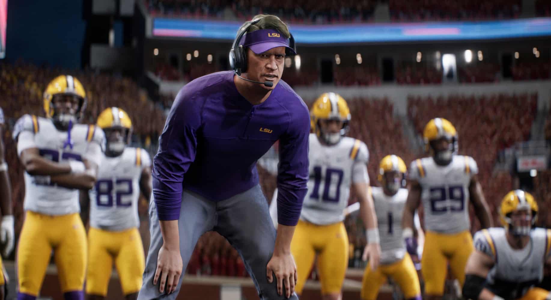 An LSU coach standing on the sideline with college football players behind him