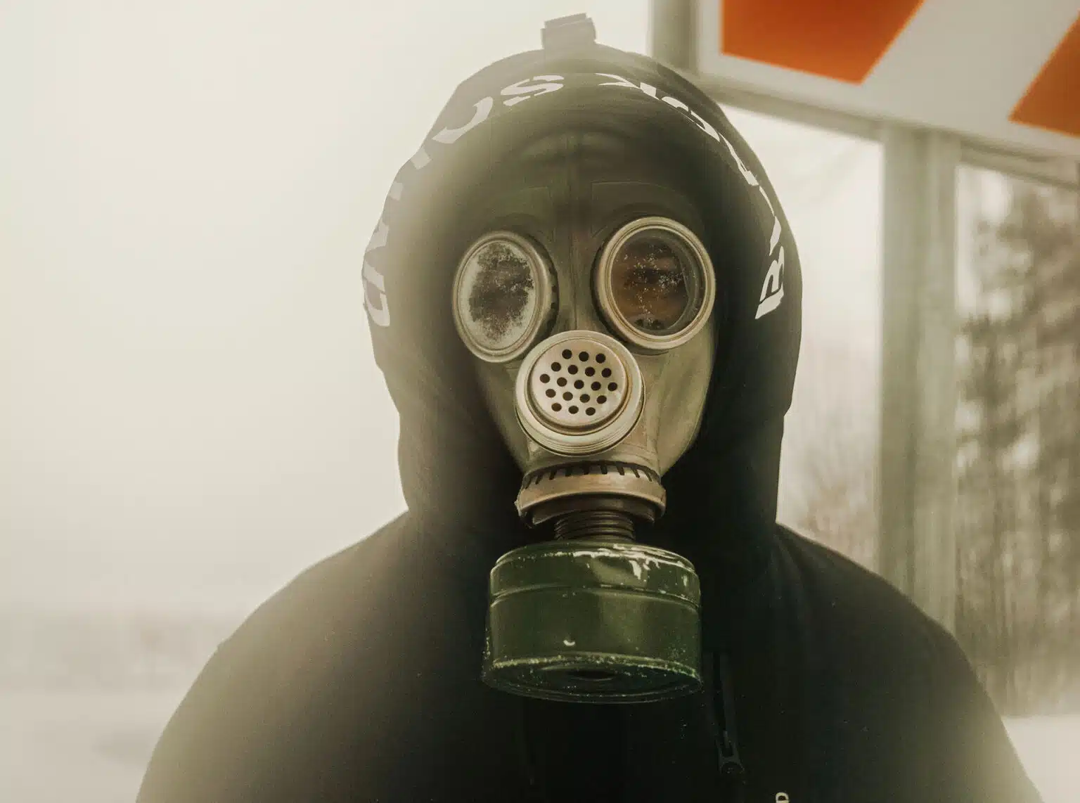 A person wearing a black hood and vintage gas mask