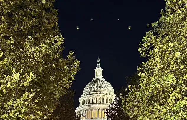 Lights in the night sky above the US Capitol, framed by trees