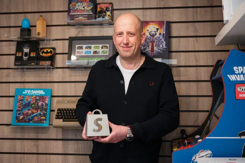 Sam Dyer, founder of Bitmap Books, standing among retro games and hardware